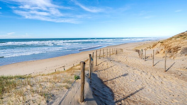 A sandy beach with a wooden fence and a clear blue sky.