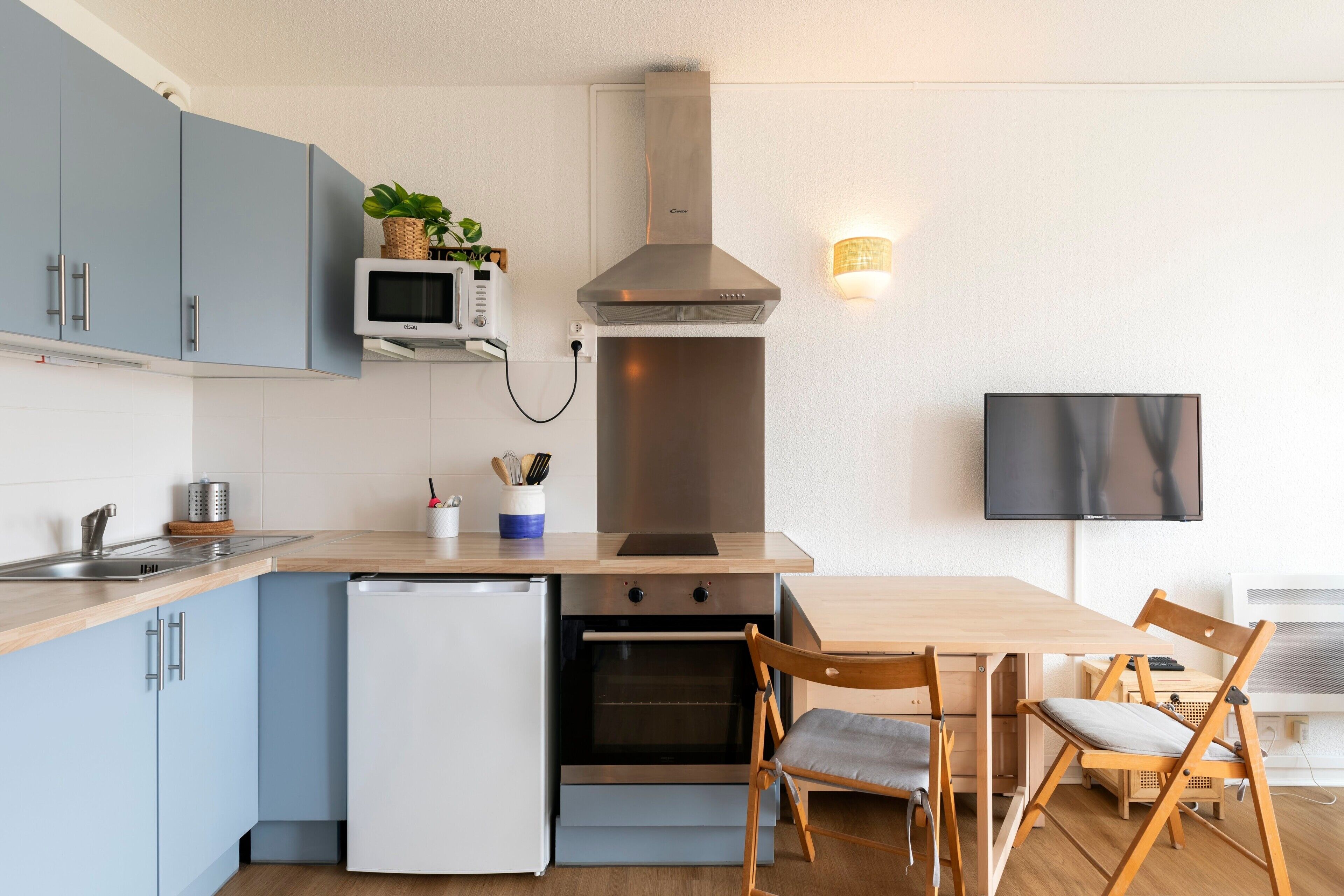 Une cuisine moderne équipée d’un four encastré, d’un four à micro-ondes et d’un téléviseur fixé au mur.