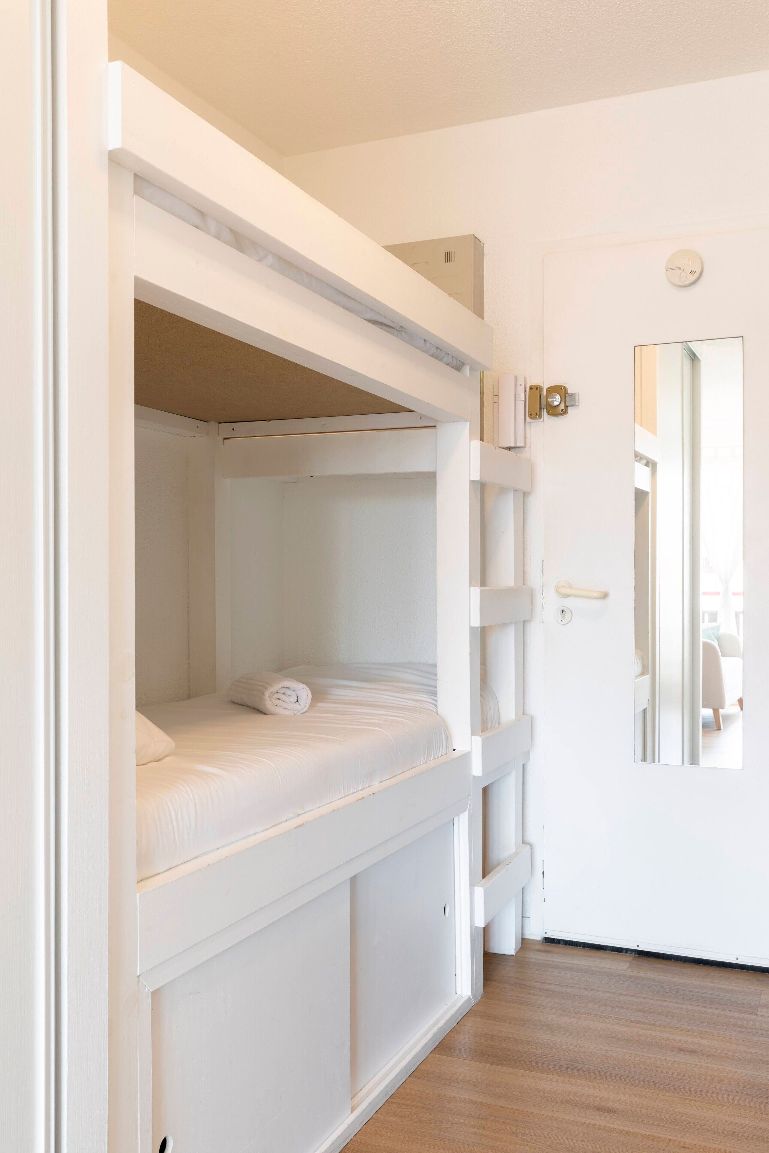 Habitación con literas, una puerta y un espejo.