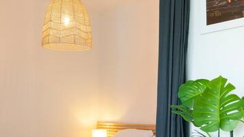 Een bed met wit beddengoed, een hanglamp, een donker gordijn en een plant in pot.