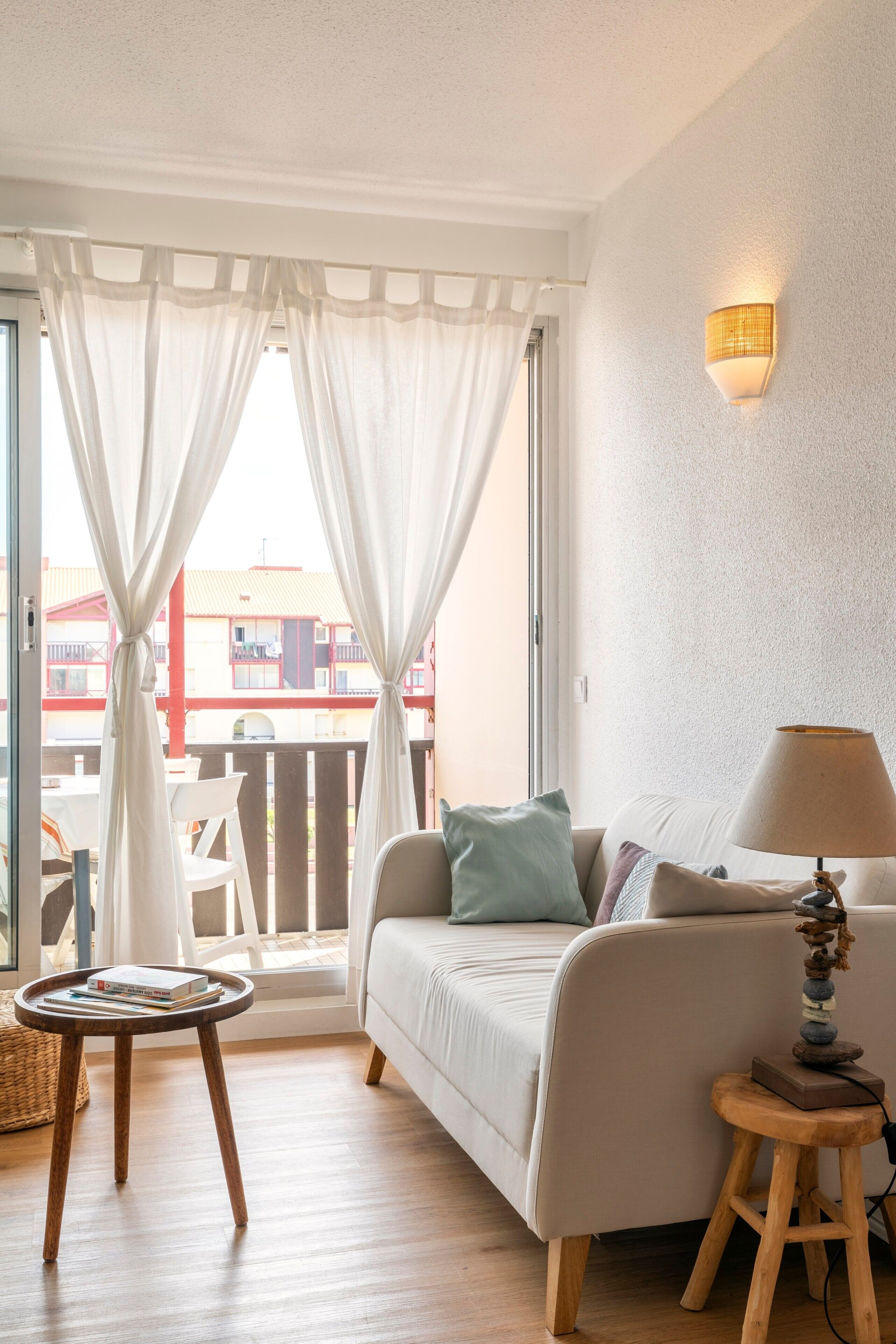 Una stanza con un letto, un tavolino con dei libri, una lampada e vista su un balcone con sedie e un edificio.