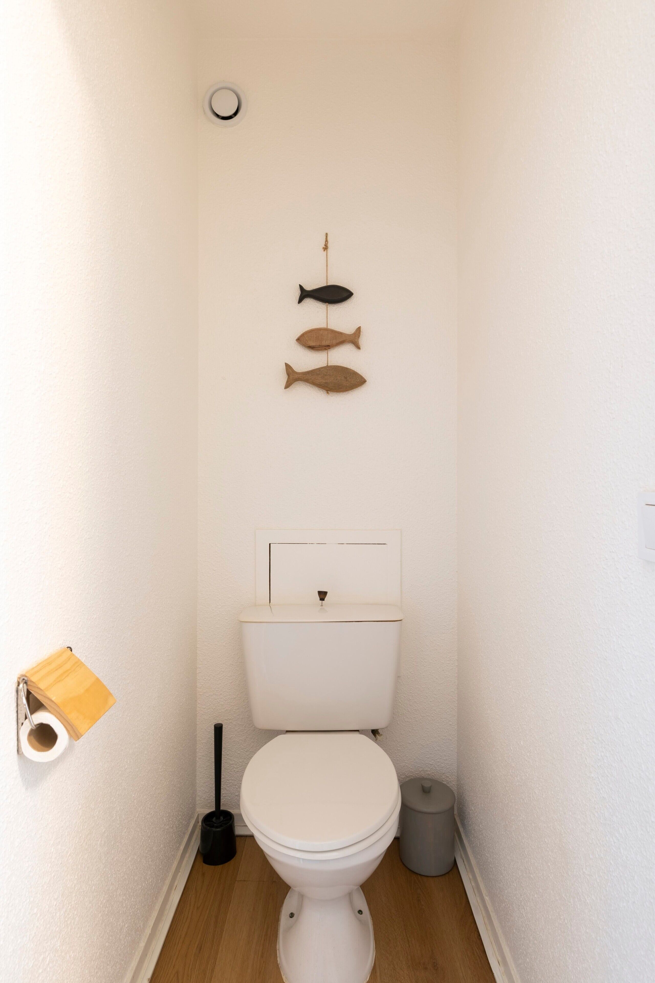 Un baño pequeño y estrecho con inodoro, dispensador de papel higiénico, bote de basura y un adorno de pez en la pared.