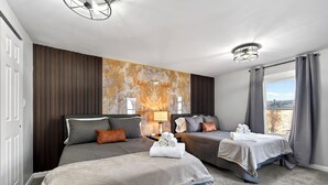 Et hotelværelse med to senge, et stort vindue med gardiner, en væg med et marmorlignende design og en loftlampe.