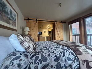 A bedroom with a bed, pillows, a wooden door, a TV, and a window. - Ski-In/Out, Discount Tyra 1 bd/1 ba-Hot tubs! (Breckenridge)