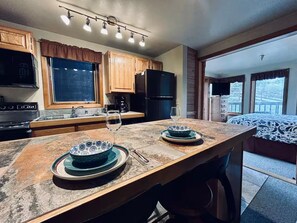 A kitchen with wooden cabinets, a black refrigerator, and a dining table set with plates and glasses. - Ski-In/Out, Discount Tyra 1 bd/1 ba-Hot tubs! (Breckenridge)