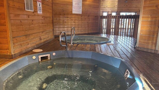 Dos jacuzzis en una cabaña de madera con terraza de madera y un cartel que indica el horario de funcionamiento.