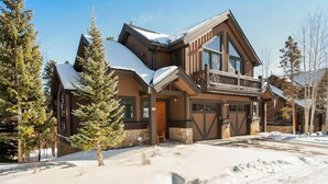 Une maison à deux étages avec un grand porche à l’avant, des portes de garage et un toit recouvert de neige.