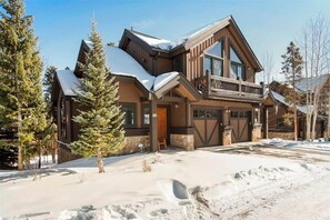 A two-story house with a large front porch, garage doors, and a snow-covered roof. - Ski~in/Ski~out~Saddlewood~3 Bd/3.5 Ba-Hot tub (Breckenridge)