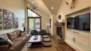 Un salon avec un canapé en cuir marron, deux fauteuils, une table basse, une cheminée, un téléviseur fixé au mur et une décoration représentant un crâne de taureau.