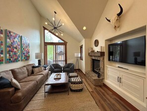 A living room with a brown leather sofa, two armchairs, a coffee table, a fireplace, a mounted TV, and a bull skull decoration. - Ski~in/Ski~out~Saddlewood~3 Bd/3.5 Ba-Hot tub (Breckenridge)