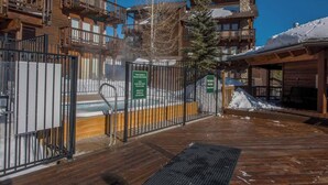 A wooden deck with a hot tub, surrounded by a wooden fence and signs indicating rules and contact information. - Ski~in~Ski~out~Tyra Aspen~2 Bd/2 Ba~Hot Tubs! (Breckenridge)