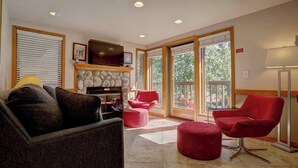 A spacious living room with a stone fireplace, red chairs, and a television. - Ski~in~Ski~out~Tyra Aspen~2 Bd/2 Ba~Hot Tubs! (Breckenridge)