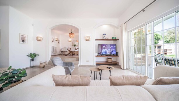 Ein großzügiger Wohnraum mit einer großen Couch, einem Fernseher und einem Essbereich im Hintergrund.