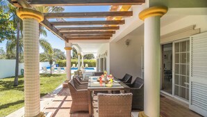 Eine Terrassengruppe mit Korbmöbeln, einer Pergola und einem Pool im Hintergrund.