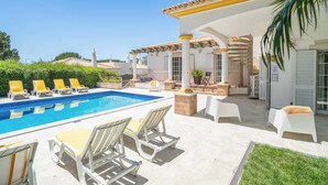 Ein Poolbereich mit Liegestühlen, einer überdachten Terrasse und Blick auf die umliegende Landschaft.
