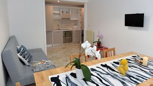 Ein modernes Wohnzimmer mit einem grauen Sofa, einem Holzesstisch mit Tischläufer mit Zeprazebra-Muster und einer Topforchidee sowie einer Kerze.