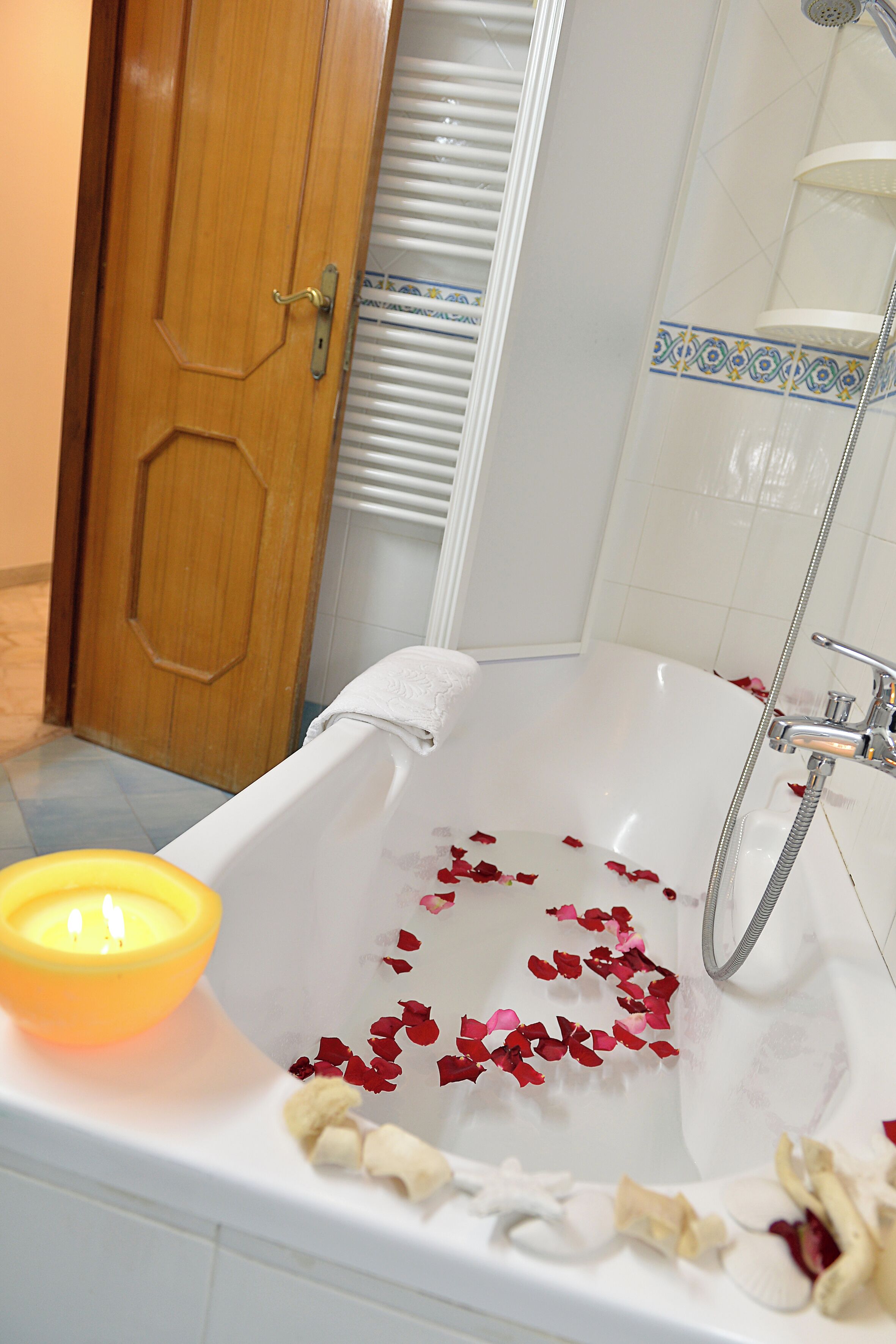 Un baño con una bañera llena de pétalos de rosa, una vela y una ducha.
