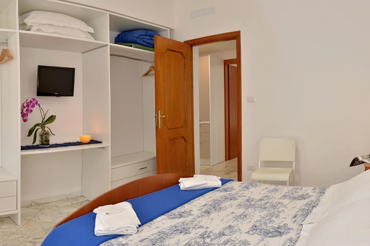 Une chambre à coucher comprenant un lit, une armoire, un miroir, une table de chevet avec une lampe et une petite plante.