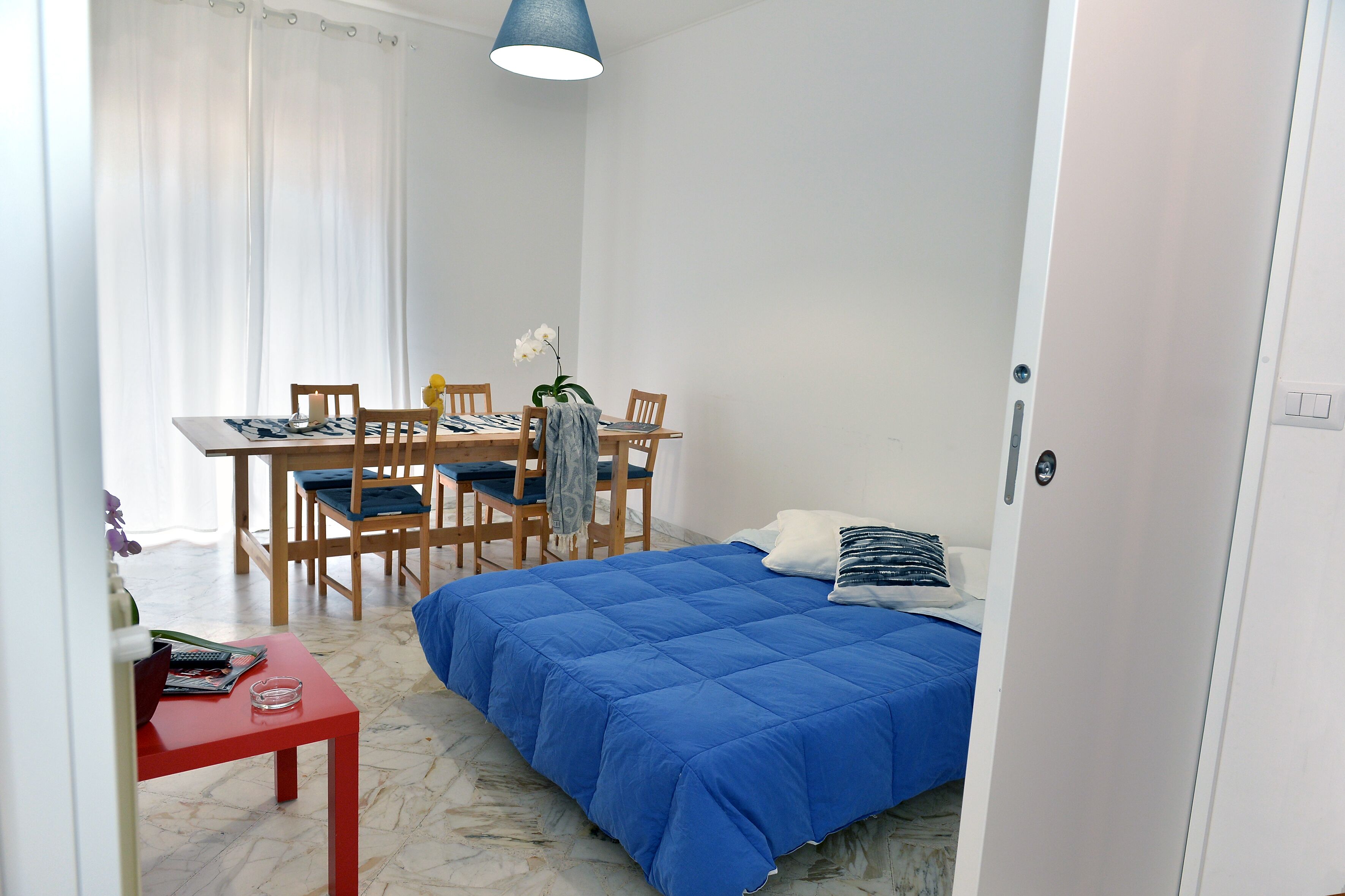 A compact bedroom with a bed, a small desk, and a dining table.