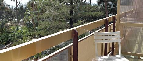 A balcony with white chairs and a table, overlooking a forested area.