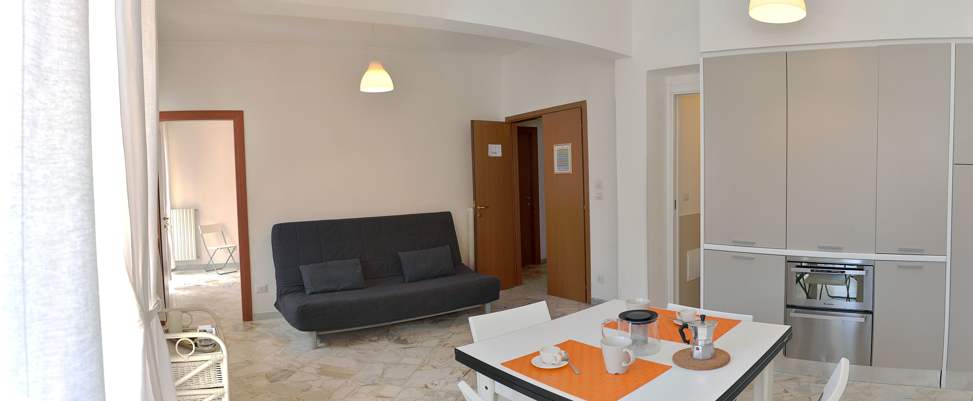 Un espace de vie compact comprenant un canapé, une table à manger avec une cafetière et un coin cuisine.