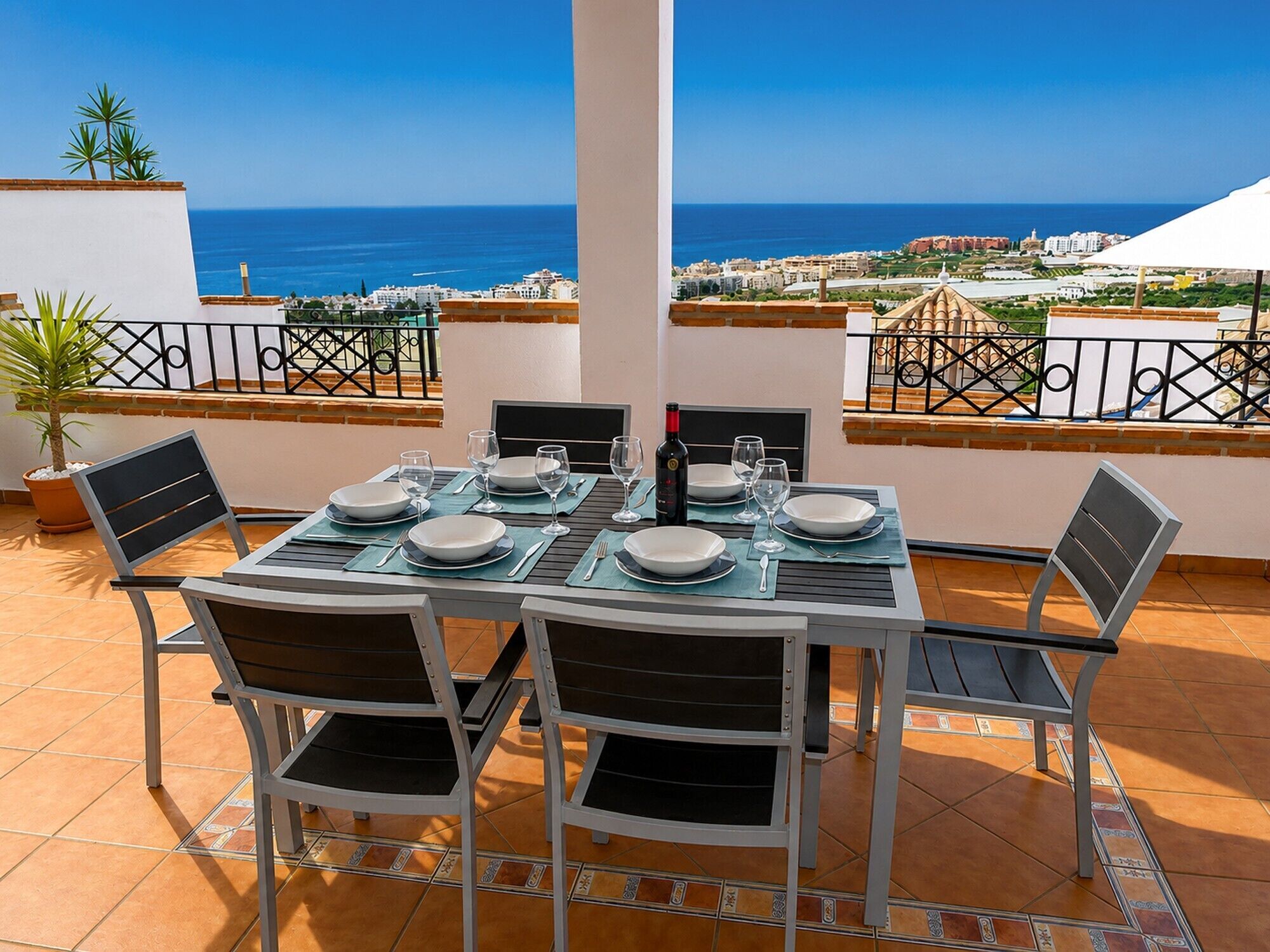 A terrace with a table set for dining, chairs, and a view of the sea.