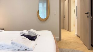 A hotel room with a neatly made bed, a large mirror, and a door leading to a hallway. - Elegant Living in Glyfada Center (Glifada)