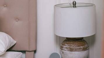 A bed with white bedding, a beige headboard, and a bedside table with a lamp and a digital device.