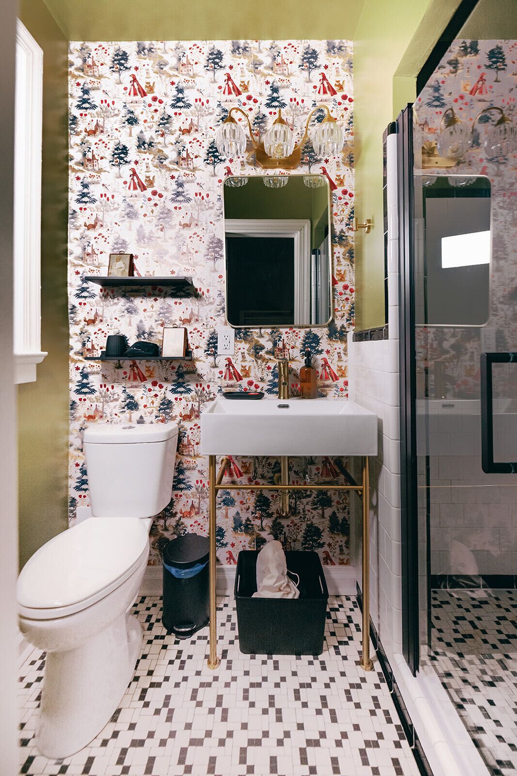 A bathroom with a toilet, sink, and mirror. The walls have a festive wallpaper with Christmas-themed illustrations.