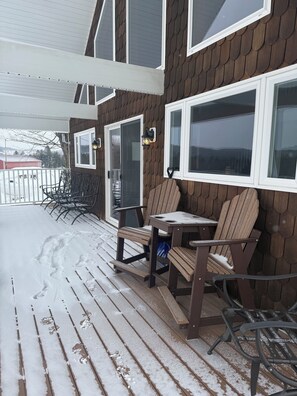 Ein überdachter Außenbereich mit Holzdeck und Stühlen, einem Tisch und Blick auf eine verschneite Landschaft.