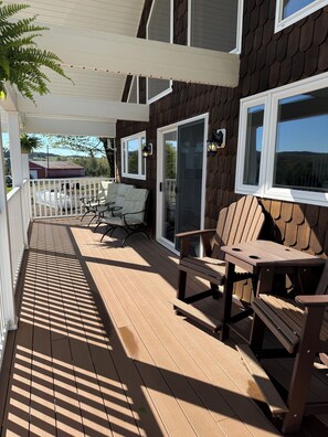 Eine überdachte Terrasse mit Holzmöbeln, einem weißen Geländer und Blick auf die umliegende Landschaft.