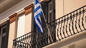 Fachada de edificio con balcón que presenta barandillas ornamentales de hierro forjado negro y un asta con bandera.