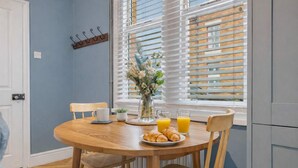 A dining area with a wooden table, chairs, a vase of flowers, croissants, and glasses of orange juice. - 4BR Home Perfect for Professionals (Beeston)