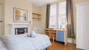 A bedroom with a bed, a desk, a chair, a fireplace, and a window with curtains. - 4BR Home Perfect for Professionals (Beeston)