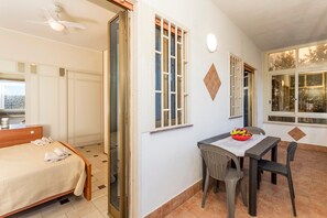 A hotel room with a bed, a dining table with chairs, a ceiling fan, and windows with curtains. - Angelina's House Apartment with Balcony and Air Conditioning (Sant'Anna)