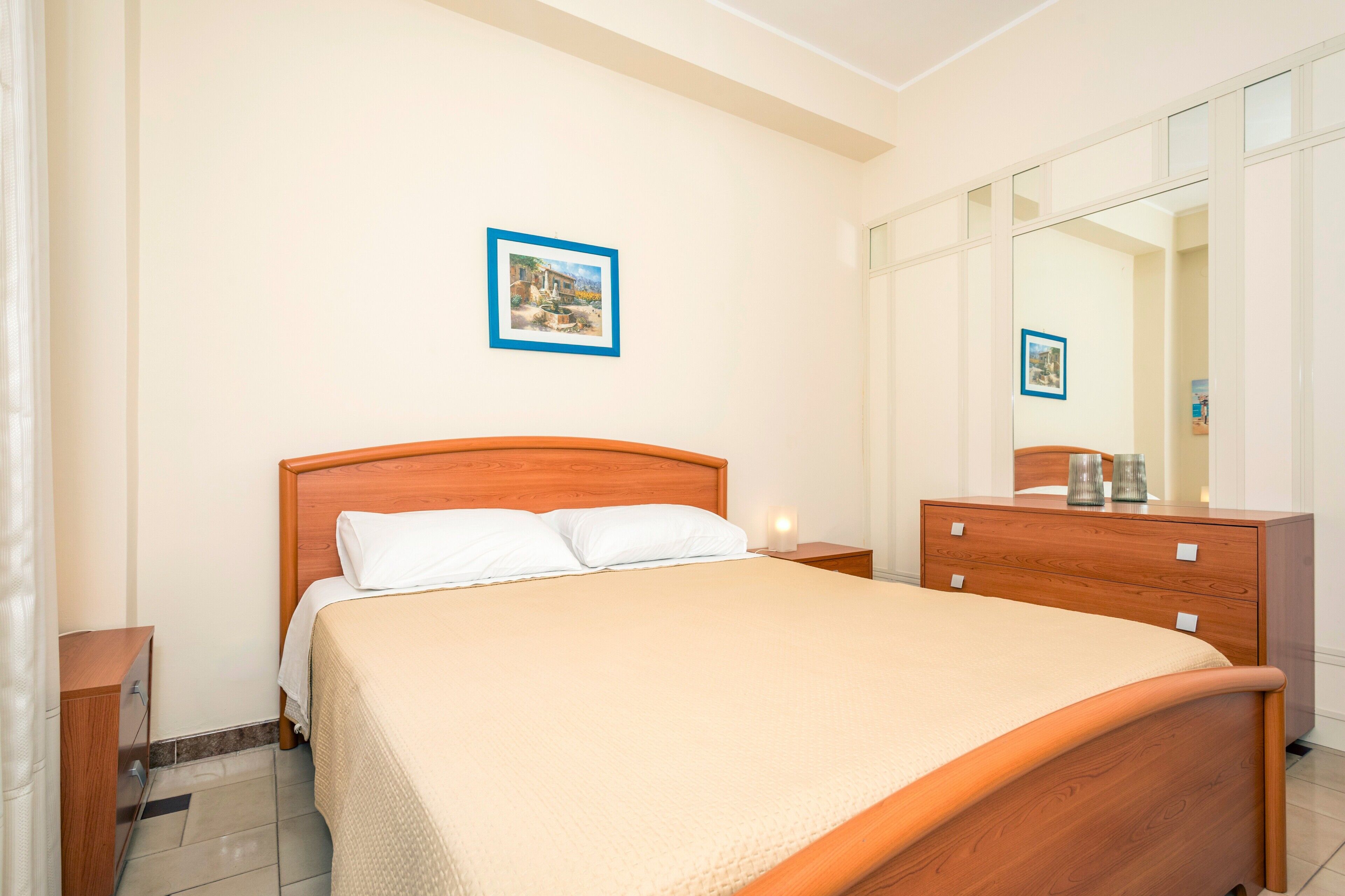 Une chambre à coucher bien rangée, avec un lit en bois, une table de chevet, une commode et un grand miroir.