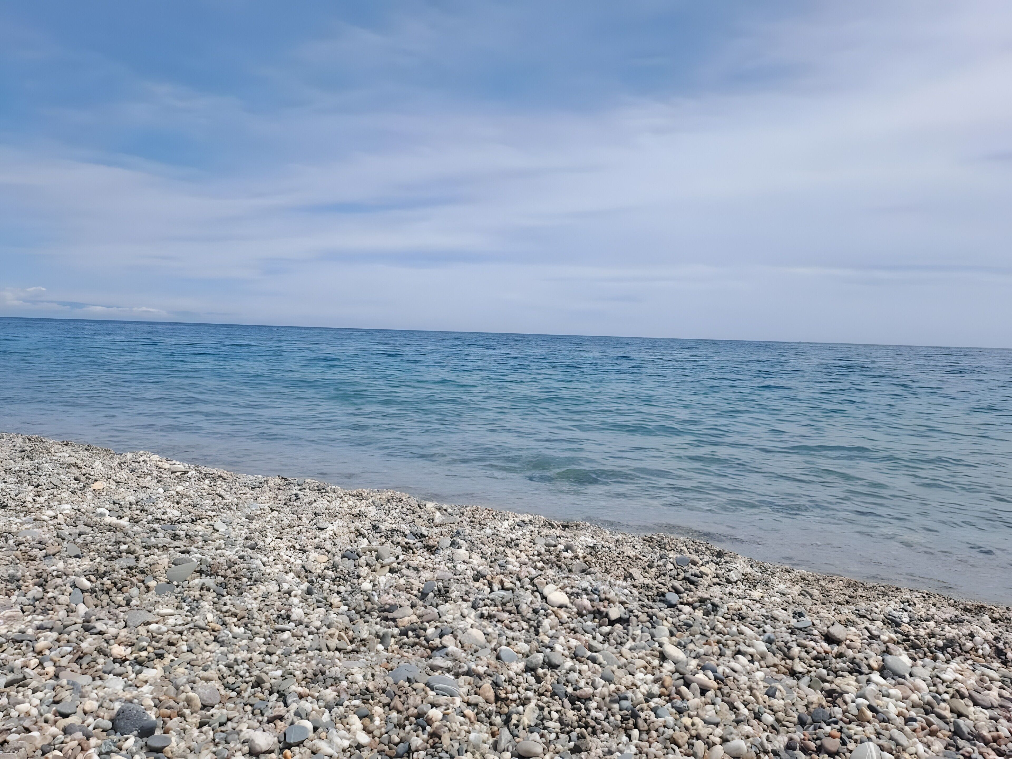 Une plage de galets, avec une mer calme et un ciel dégagé.
