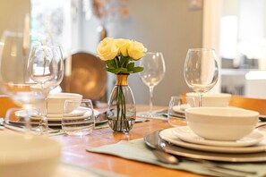 A dining table set with plates, bowls, and wine glasses, accompanied by a vase of yellow roses. - Hillside House in Henley (Oxfordshire)