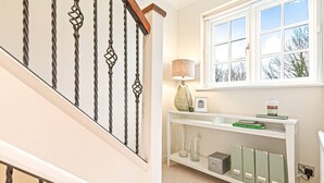 A staircase with a white railing and a wall-mounted shelf with books and decorative items. - Hillside House in Henley (Oxfordshire)