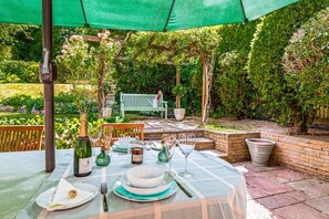An outdoor dining area with a table set for four, surrounded by greenery and a wooden bench. - Hillside House in Henley (Oxfordshire)