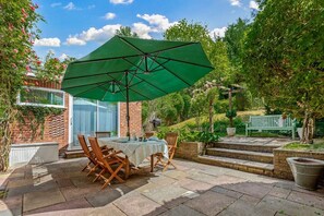An outdoor patio with a table and chairs, a green umbrella, and a brick wall. - Hillside House in Henley (Oxfordshire)