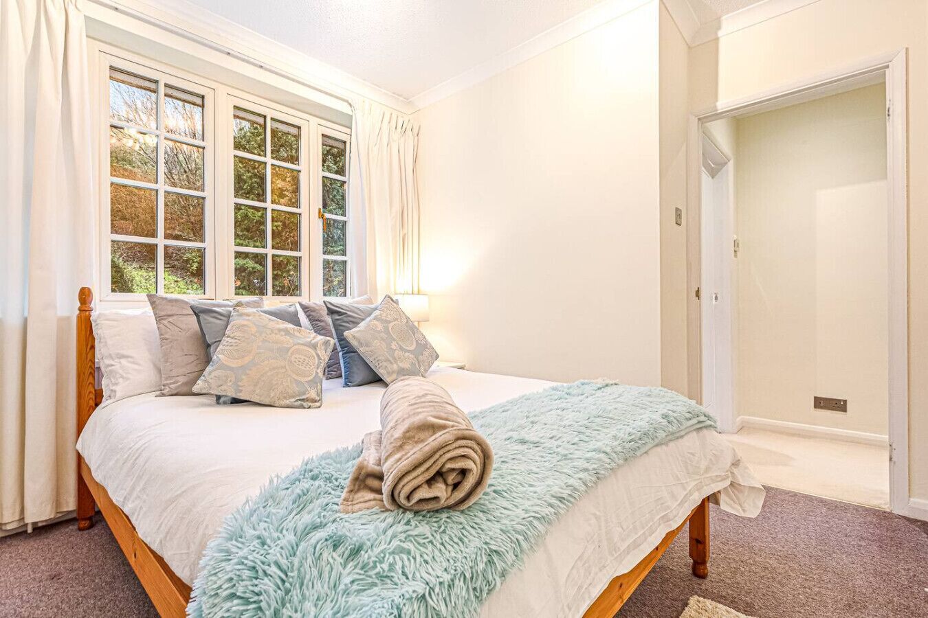 A bedroom with a large bed, a window with curtains, a fluffy rug, and a door.