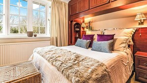 A bedroom with a large bed, wooden headboard, and a window with curtains. - Hillside House in Henley (Oxfordshire)
