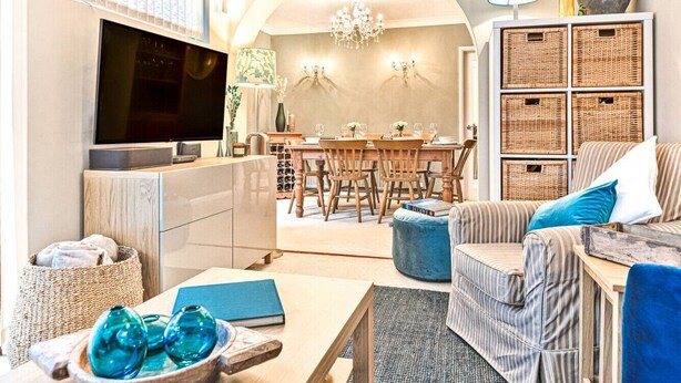 A modern living room with a TV, dining area, and a cozy seating area with a sofa and ottoman. - Hillside House in Henley (Oxfordshire)