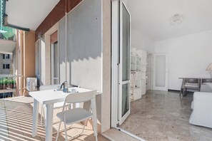 Quarto com uma mesa e cadeiras brancas, uma porta de vidro deslizante, um armário branco e uma cama.