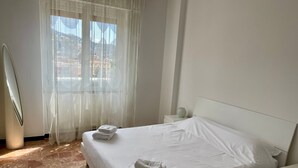 Ein Hotelzimmer mit Bett, Nachttisch, einer Vase und einem Fenster mit transparenten Vorhängen.