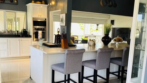 Een moderne keuken met witte kasten, een centraal eiland met barkrukken, en een eethoek met een tafel met glazen blad.