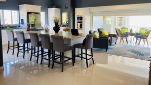 Een moderne keuken met een centraal eiland, barstoelen en een eethoek met stoelen en een tafel.