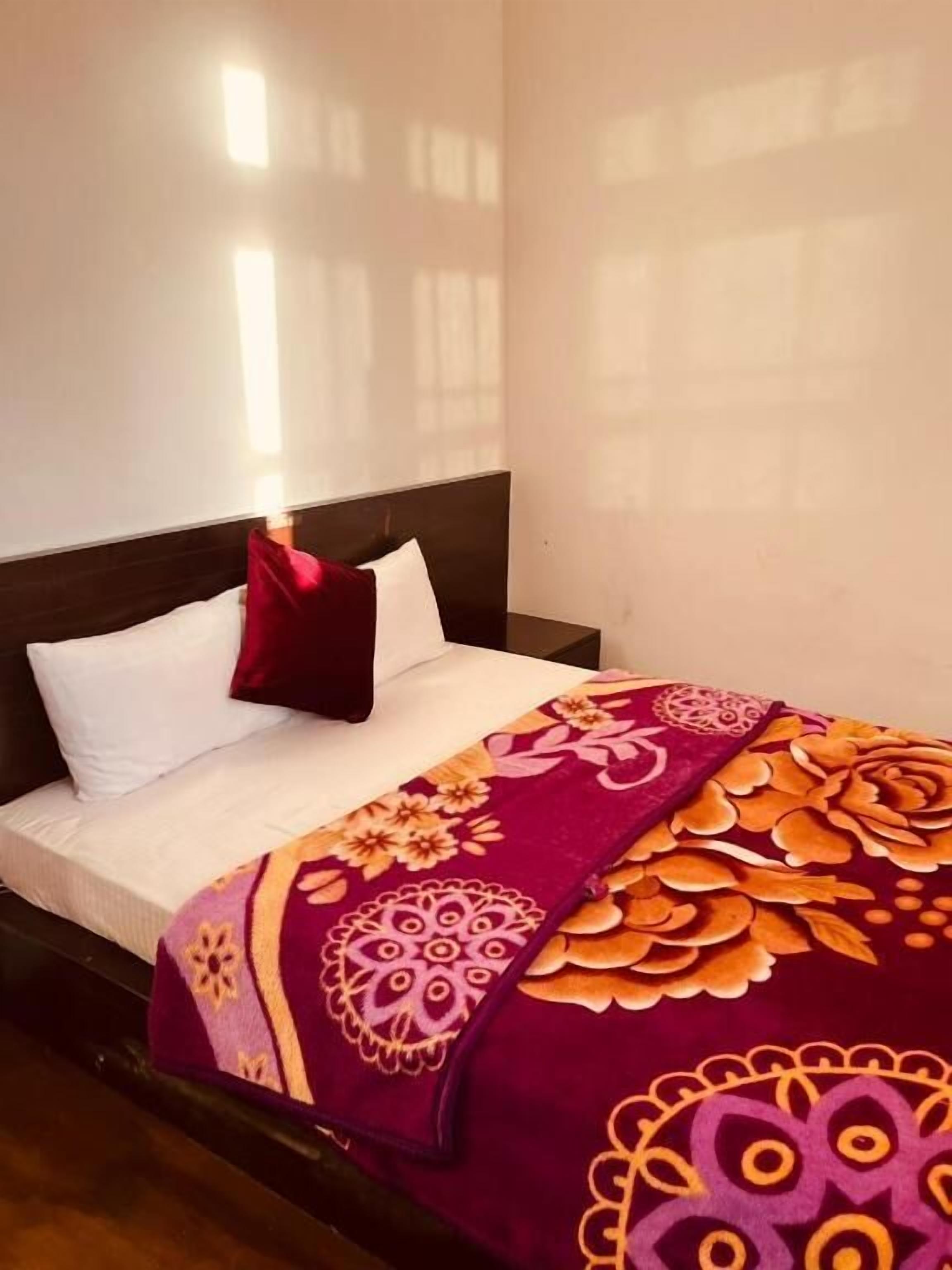 A bed with a dark headboard, white pillows, and a colorful floral bedspread.