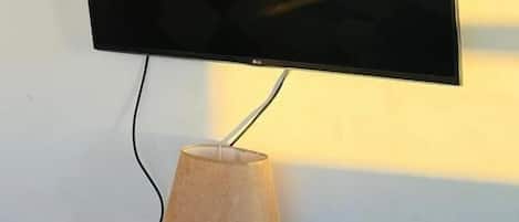 A flat-screen TV mounted on a white wall with a cactus-shaped lamp below it.